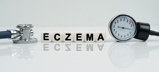 On a reflective white surface lies a stethoscope and cubes with the inscription - ECZEMA