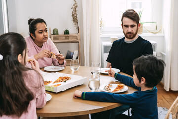 Mixed family sitting at the table and eating vegan pizza with natural ingredients at home. Vegan...