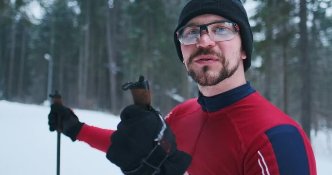Happy skier talks. Young man in red ski suit stands on the cross country ski track talks and laughs and looks into the camera