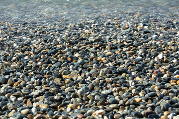 Multicolored pebble stones, covered with a sea wave from above. Horizontal photo