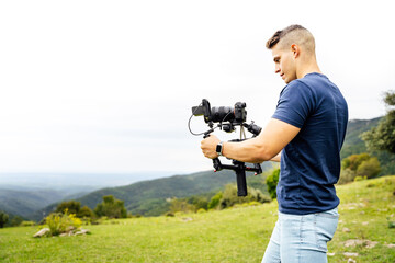 Young muscular Caucasian man manning a camera on top of a gimbal while working recording a scene in the middle of a field. Videomaker with steadicam and professional team working.