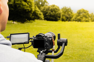 Stabilized camera on a gimbal / steadicam recording a scene. Photograph taken from behind and up close while the operator operates the camera.