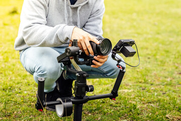 Camera operator adjusting the automatic camera stabilizer on a green lawn. Creation of videos with...