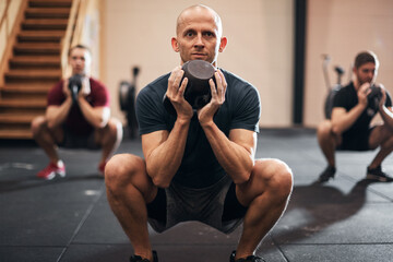 Obraz premium Fit man doing squats with weights during a gym class