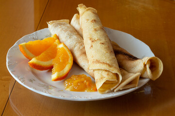 Crepes with orange jam and oranges  - wooden background