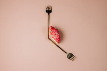 Intermittent fastin concept. One-third donut symbolizing eight hours with cutlery like a clock hands on pink background.