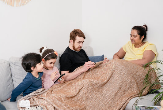 Young mixed-race family relaxing at home with digital devices. Real life, diversity, digital technology