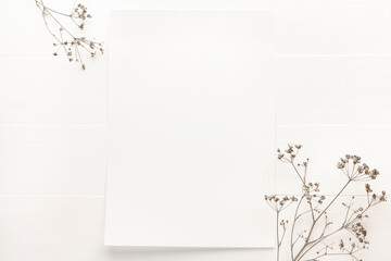 Blank sheet of paper mockup on white wooden background with dry flowers. Empty poster mock up top...