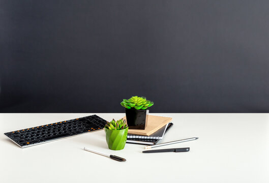 White home office table with copy space on black background. Computer notepads and succulent flowers. Keyboard stationery at home office workplace for remote work.