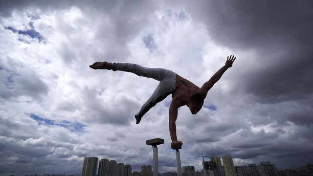 Flexible male circus Artist turning and keep balance by one hand on the rooftop against amazing cloudscape. Movement, motion and control concept 