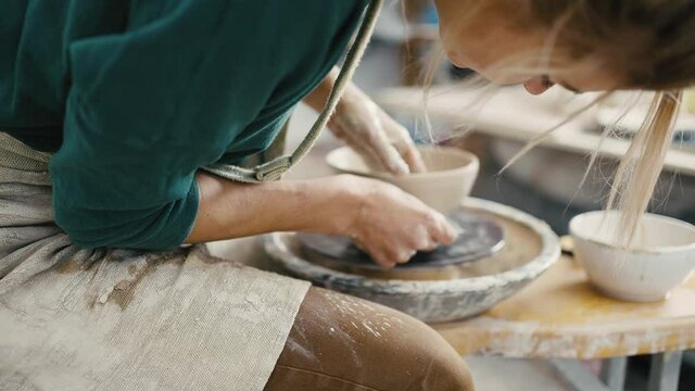 Zoom out shot of woman potter making ceramic crockery on pottery wheel, slow motion