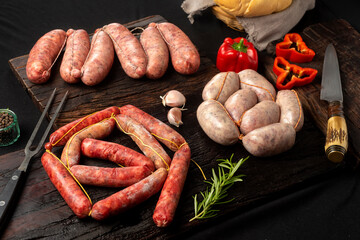 Beef and pork sausages, sausage and raw sausages on wooden board with vegetables, pepper, garlic,...
