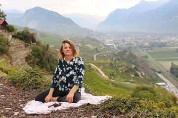 Naklejka premium Woman sitting on the white cloth on the ground where there are some fresh ripe grapes, background has spectacular view of Mountains.Wine production region. Green landscape.