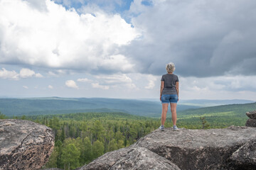 A middle-aged woman at the top of the mountain enjoys a stunning view of the hilly valley. Healthy lifestyle. Copy space