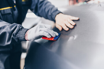 Car wrapping specialist putting vinyl foil or film on car. Selective focus.