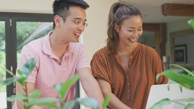 Smiling Asian couple sitting at table at home reviewing domestic finances using laptop - shot in slow motion