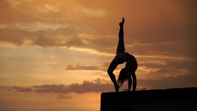 Flexible girl doing handstand on sky background during dramatic sunset in slow motion 
