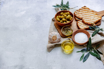 Mediterranean olives with herbs and bread slices on rustic table, top view