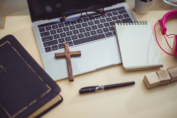 Cross on bible with headset and laptop in online study bible concept.