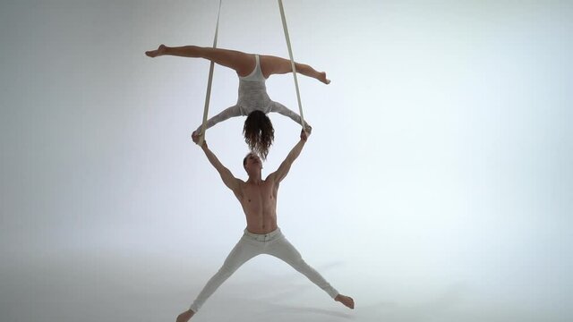 Aerial straps duo wearing white costume on white background doing performance 