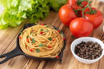 Italian pasta in a frying pan on a light wooden background with seasonings and vegetables.