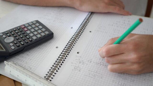 Hand Solving Algebraic Problem On A Math Notebook With Scientific Calculator On The Side. close up, high angle