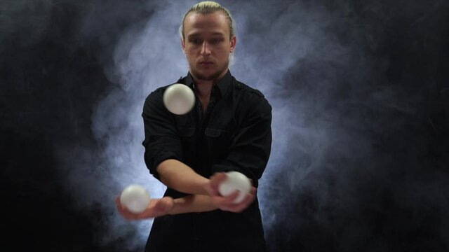 Man in black juggling white balls. Concentration, ability, speed, reaction