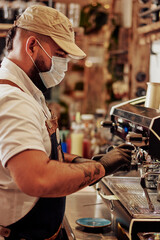 Hombre joven con tatuaje y tapaboca en maquina de expresso sirviendo un cafe
