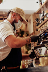 Hombre joven con tatuaje y tapaboca en maquina de expresso sirviendo un cafe