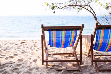 Deck chair or wooden beach chaise longue on sand beach with blue sea and tree at coast. for sitting and resting of tourist in travel summer holidays.