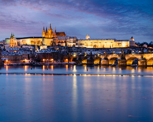 .Charles Bridge on the Vltava River and Prague Castle and the Church of St. Vitus in winter and snow on the roofs in the center of Prague in the early evening