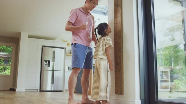 Excited Asian girl being measured by father at home against oversized ruler - shot in slow motion