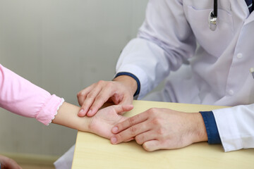 asian man  doctor talks to little girl patient in hospital office while examining the patients pulse by hands