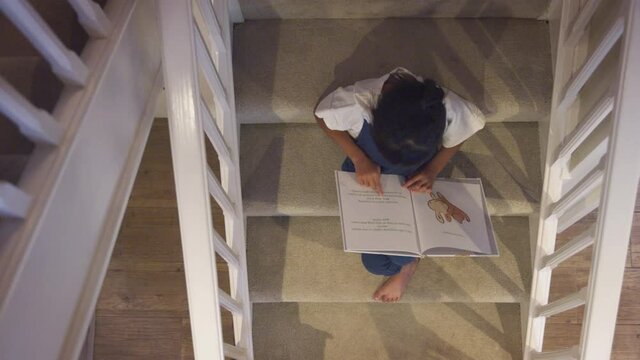 Overhead View Of Asian Girl Sitting On Stairs At Home Reading Book - Shot In Slow Motion