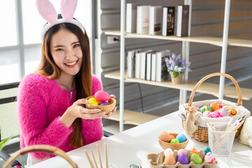 Easter holiday concept, Happy Asian Young woman show holding a basket with colorful Easter eggs In the white room background