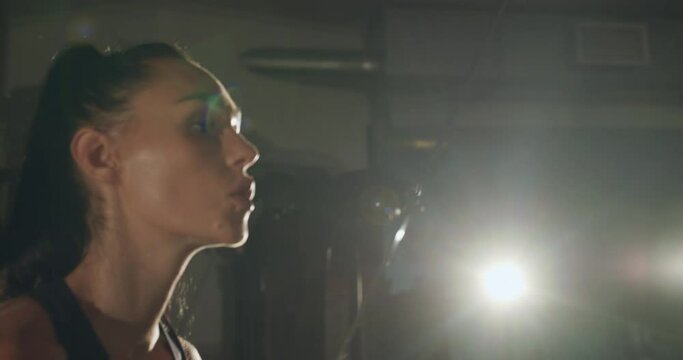 Attractive athletic, sweaty girl pulls loops in a dark gym with backlit