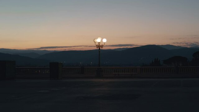 Empty parking lot with a street light in a morning dawn. Hills and trees in the background. Orange sky, rustic fense overlooking Florence city in Tuscany. 4K, 50fps, slow motion, smooth gimbal shot.