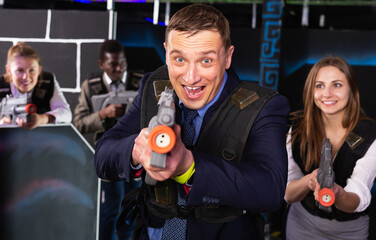 Emotional portrait of businessman playing laser tag with his co-workers on dark labyrinth