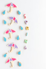 A vertical row of umbrella sugar cookies with raindrops against a white background. A spring concept.