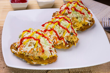 Plato de comida venezolana hecho de tostón con ensalada de col, queso rallado, carne mechada,...