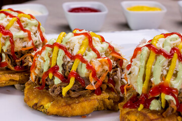 Plato de comida venezolana hecho de tostón con ensalada de col, queso rallado, carne mechada, pollo y cremas en plato blanco para restaurantes.