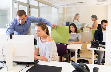 Obraz premium Male and female colleagues discussing online project looking at pc screen in busy office. Focus on man