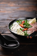 Traditional vietnamese soup Pho Bo with beef and noodles on a wooden background, selective focus