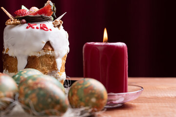 Easter cake, colored eggs and a burning candle on a dark background