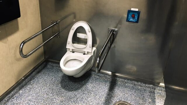 disabled toilet with a white toilet seat standing up against the silver wall equipped with armrests at a ferry. Slowly panning dolly shot.