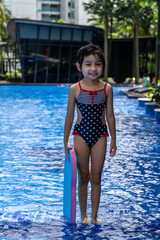 Cute little girl preparing for her swimming lesson in the pool while holding a kick board