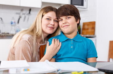 Portrait of happy woman and her son doing homework at kitchen
