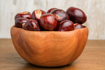 Buckeye Chestnut in wooden bowl on wooden surface. Side View formation of Fresh conkers.