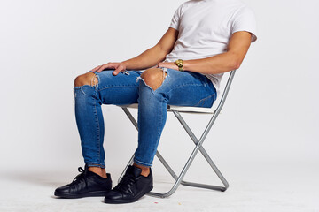 Fototapeta na wymiar a man in jeans and a t-shirt sits on a chair on a light background side view
