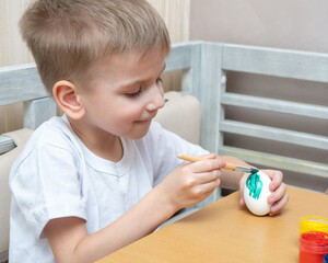 Easter eggs coloring concept. Happy caucasian boy sits at the table and paints eggs for Easter. Preparing to celebrate Easter concept